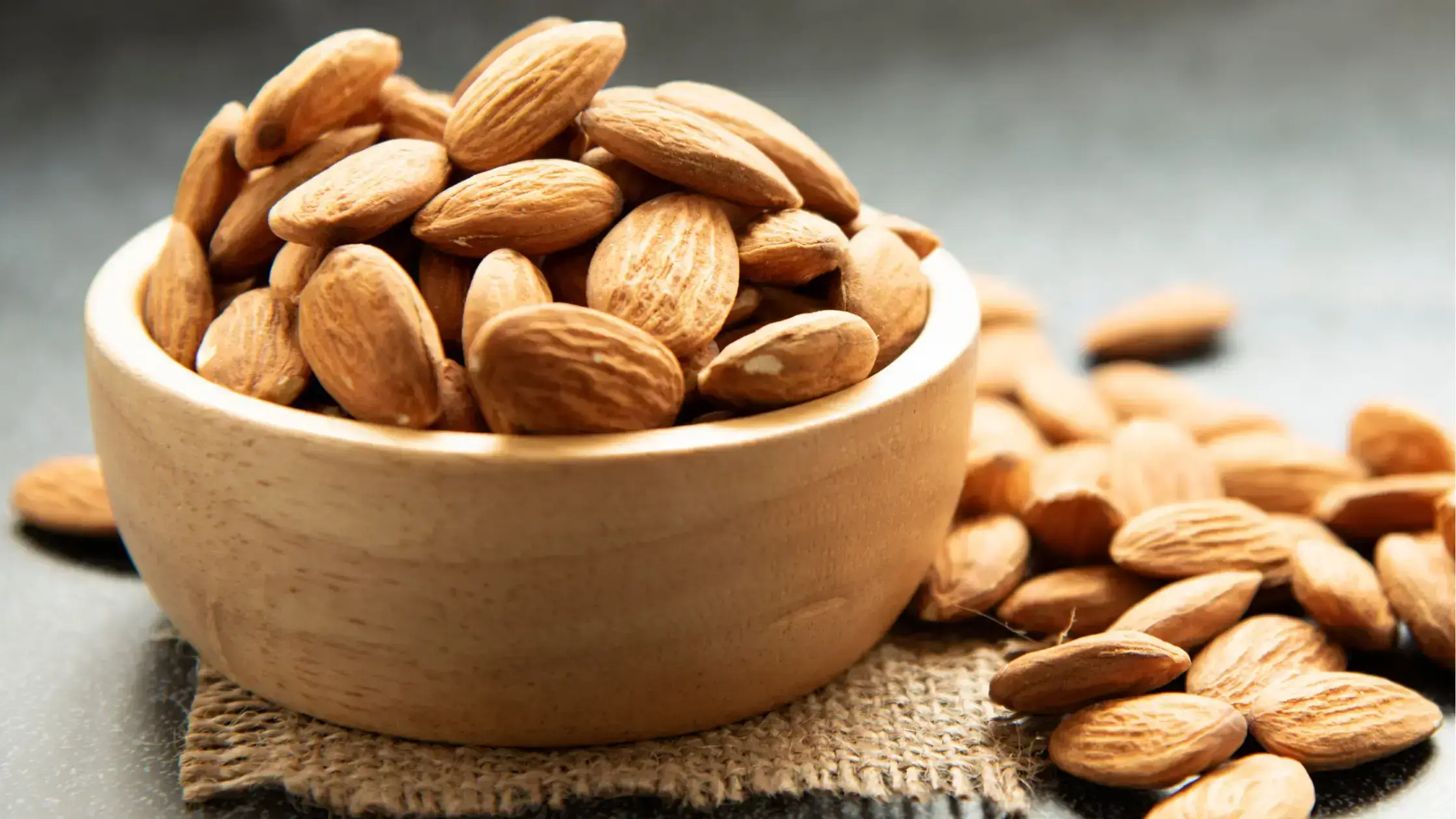 Un bol en bois rempli d'amandes, avec des amandes éparpillées autour.