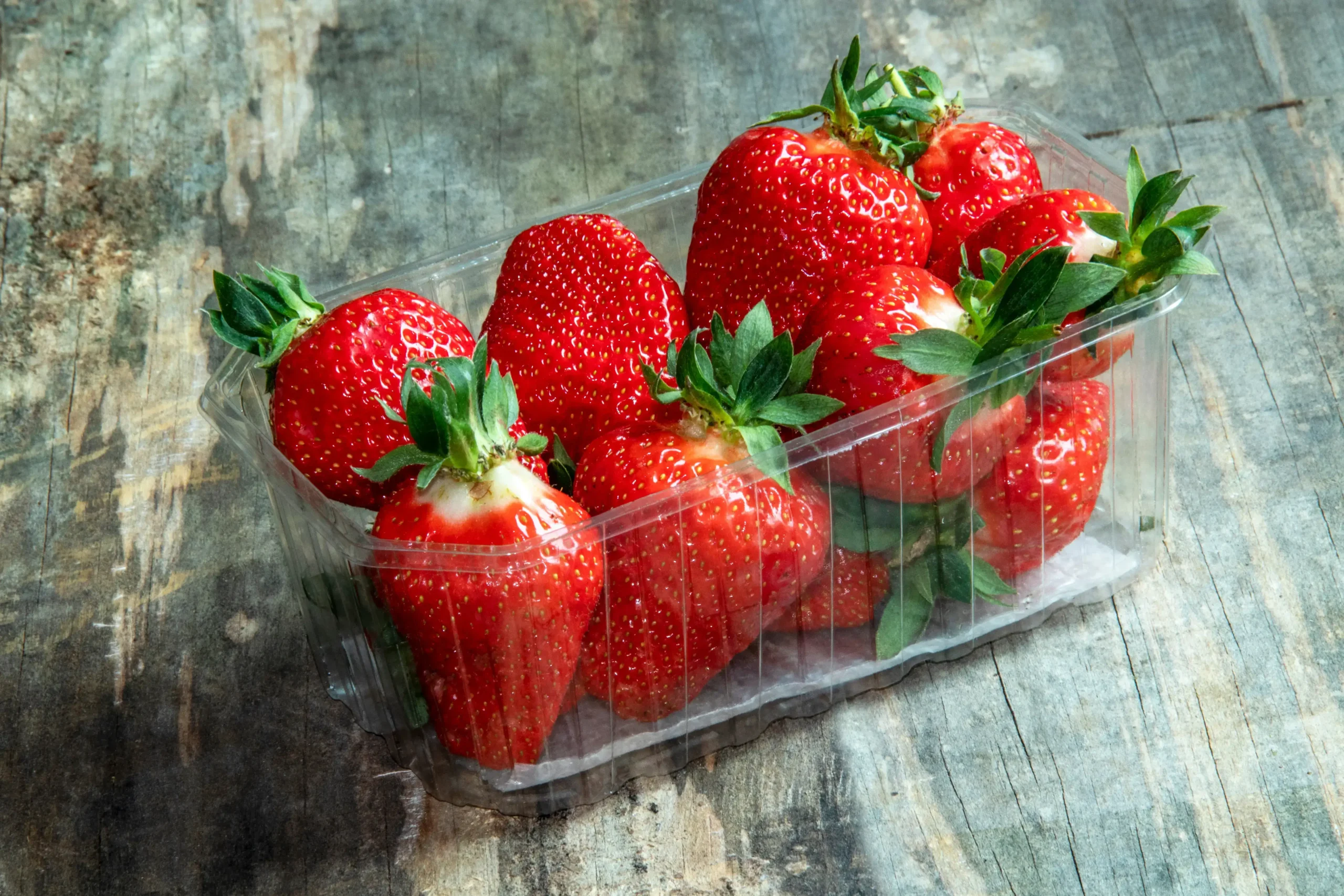 Un barquette de fraises fraîches sur une surface en bois.
