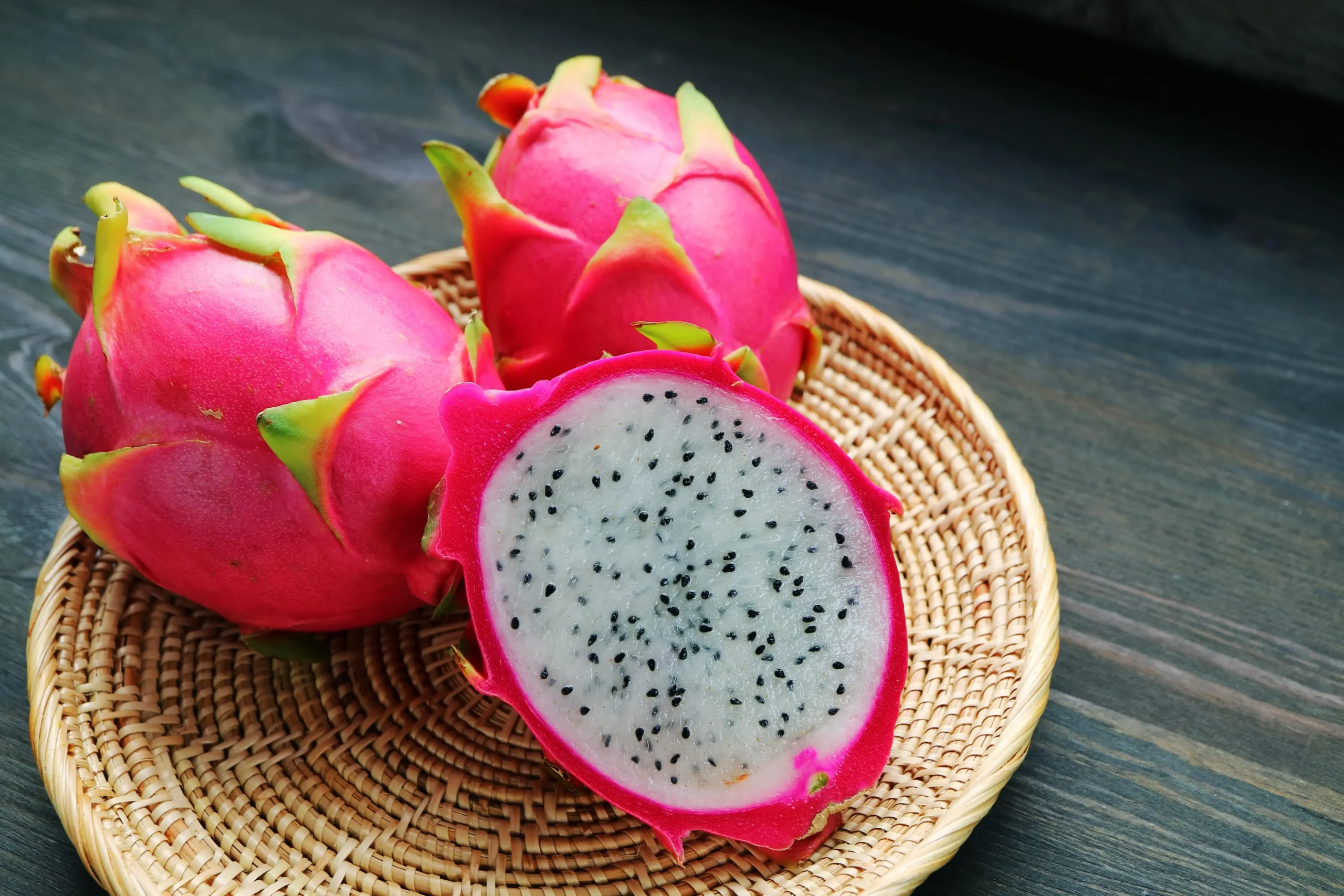 Un fruit du dragon coupé en deux, avec des fruits entiers en arrière-plan.