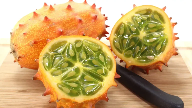 Kiwano coupé en deux révélant sa chair verte gélatineuse et ses graines, avec un couteau noir sur une planche en bois.