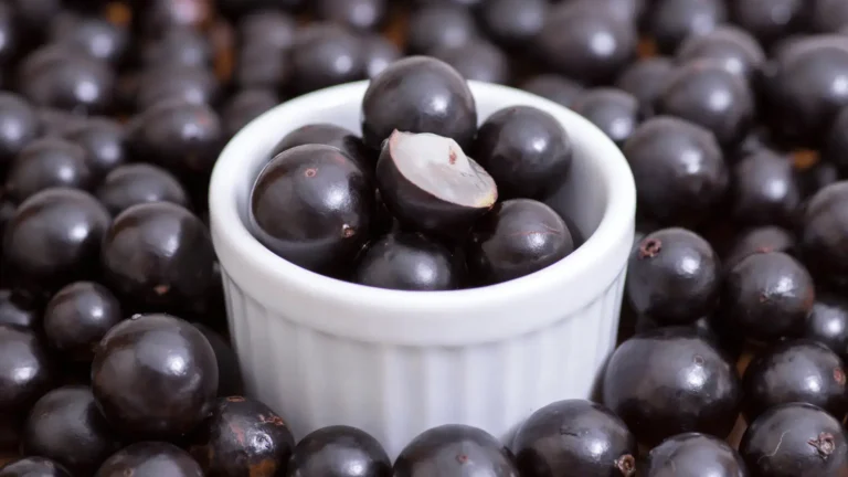 Un bol blanc rempli de jabuticaba, entouré de nombreux fruits noirs.