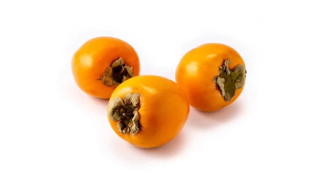 Trois kakis orange vif avec leur calice sec, posés sur un fond blanc.