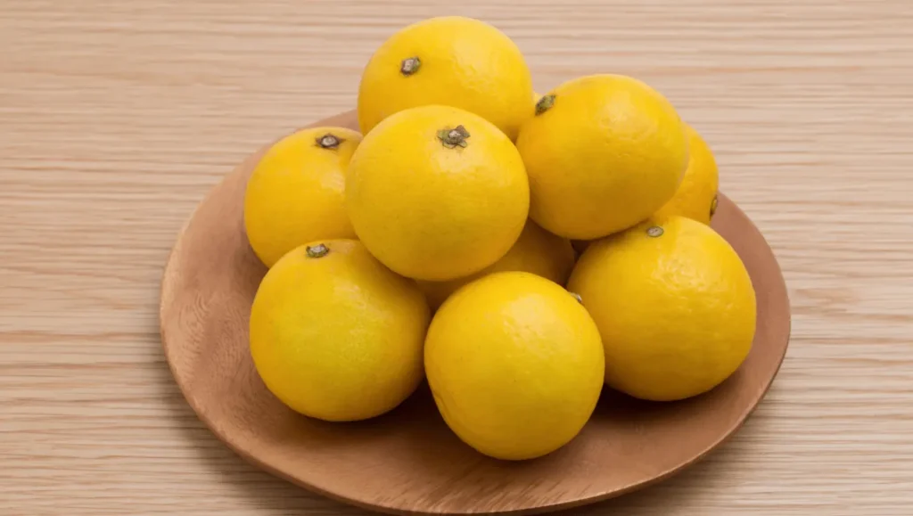 Fruits de Hyuganatsu jaunes et brillants disposés sur un plateau en bois.