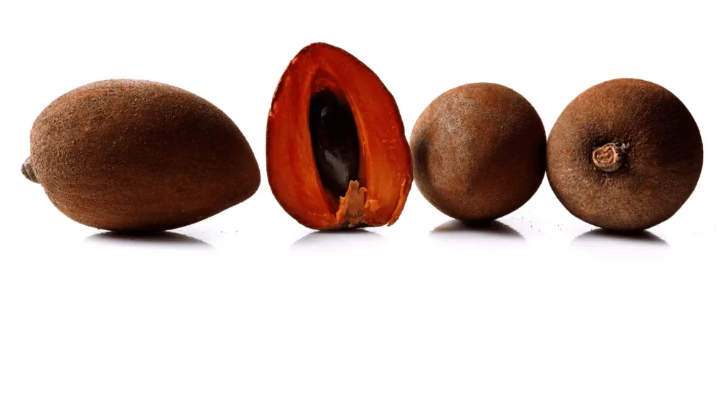 Quatre fruits de mamey alignés sur un fond blanc, dont un ouvert exposant sa chair orangée et son noyau noir lisse.