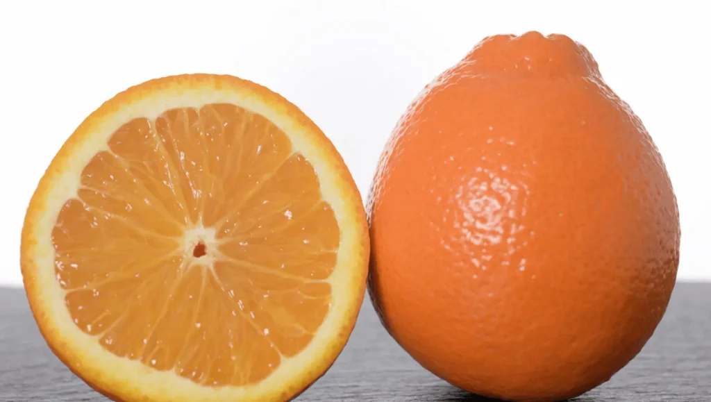Une Minneola orange vif avec une bosse caractéristique sur le dessus, accompagnée d’une moitié coupée exposant sa chair juteuse et ses quartiers bien définis.