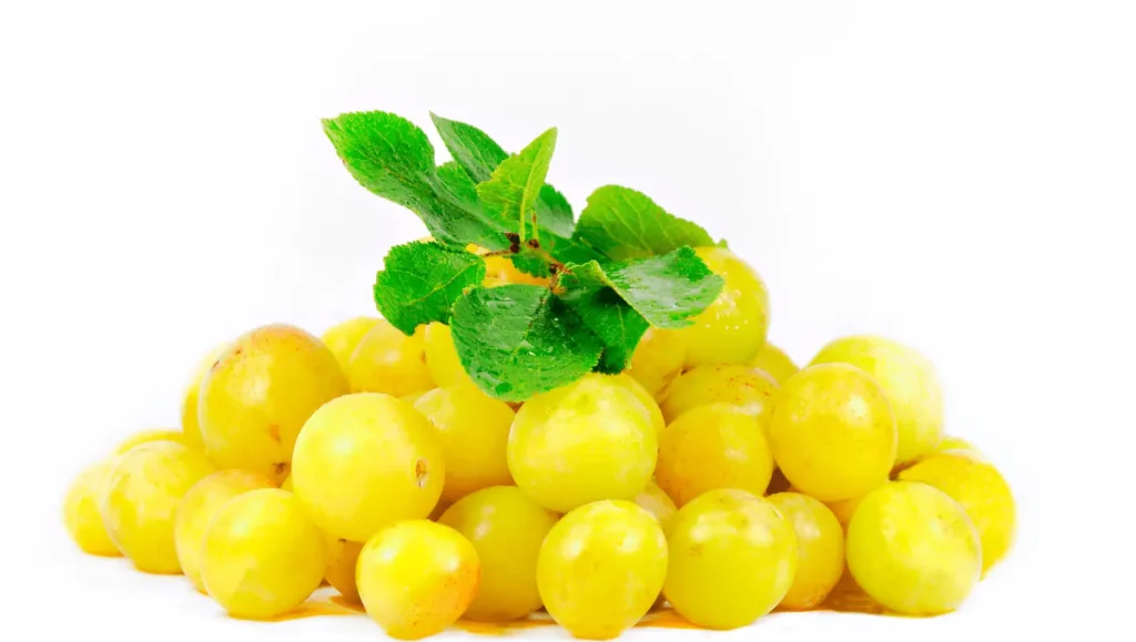 Un amas de mirabelles dorées et brillantes surmontées de feuilles vertes, avec un arrière-plan blanc lumineux.