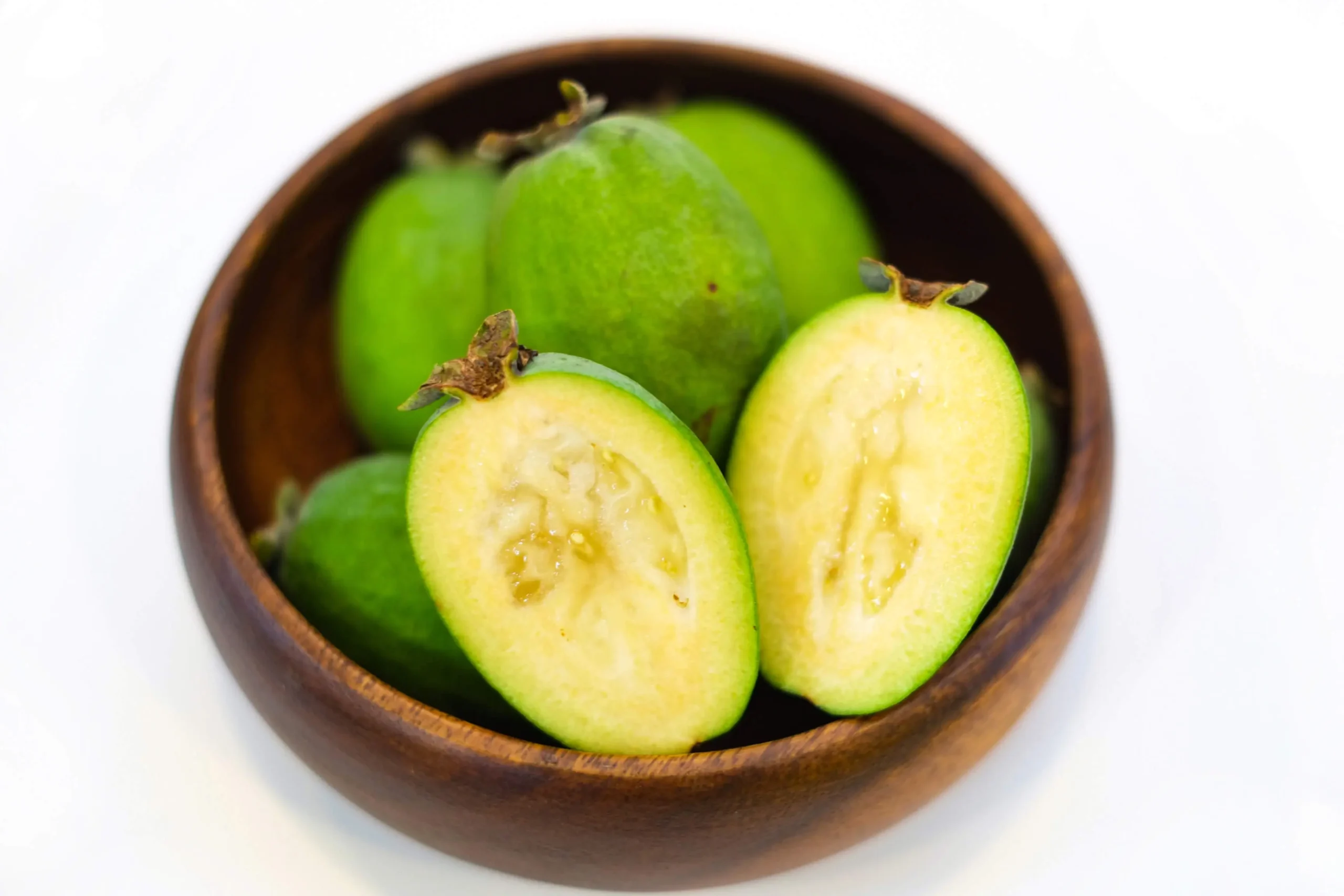 Bol en bois rempli de feijoas vertes, avec un fruit coupé en deux montrant sa chair juteuse et granuleuse.
