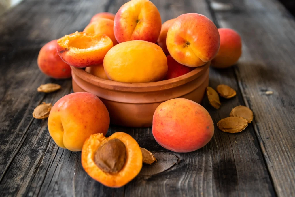 Bol en terre cuite rempli d’abricots mûrs, avec quelques fruits coupés en deux et des noyaux éparpillés sur une table en bois.