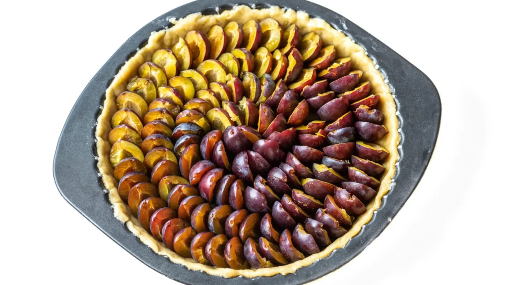 Tarte crue dans un moule rond, avec des prunes coupées en quartiers et disposées en spirale colorée.