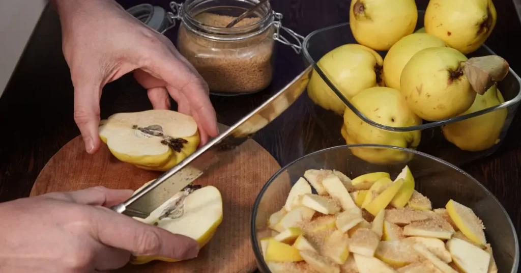 Une personne coupe des coings sur une planche en bois, avec des tranches sucrées dans un bol et des fruits entiers dans un saladier à côté.