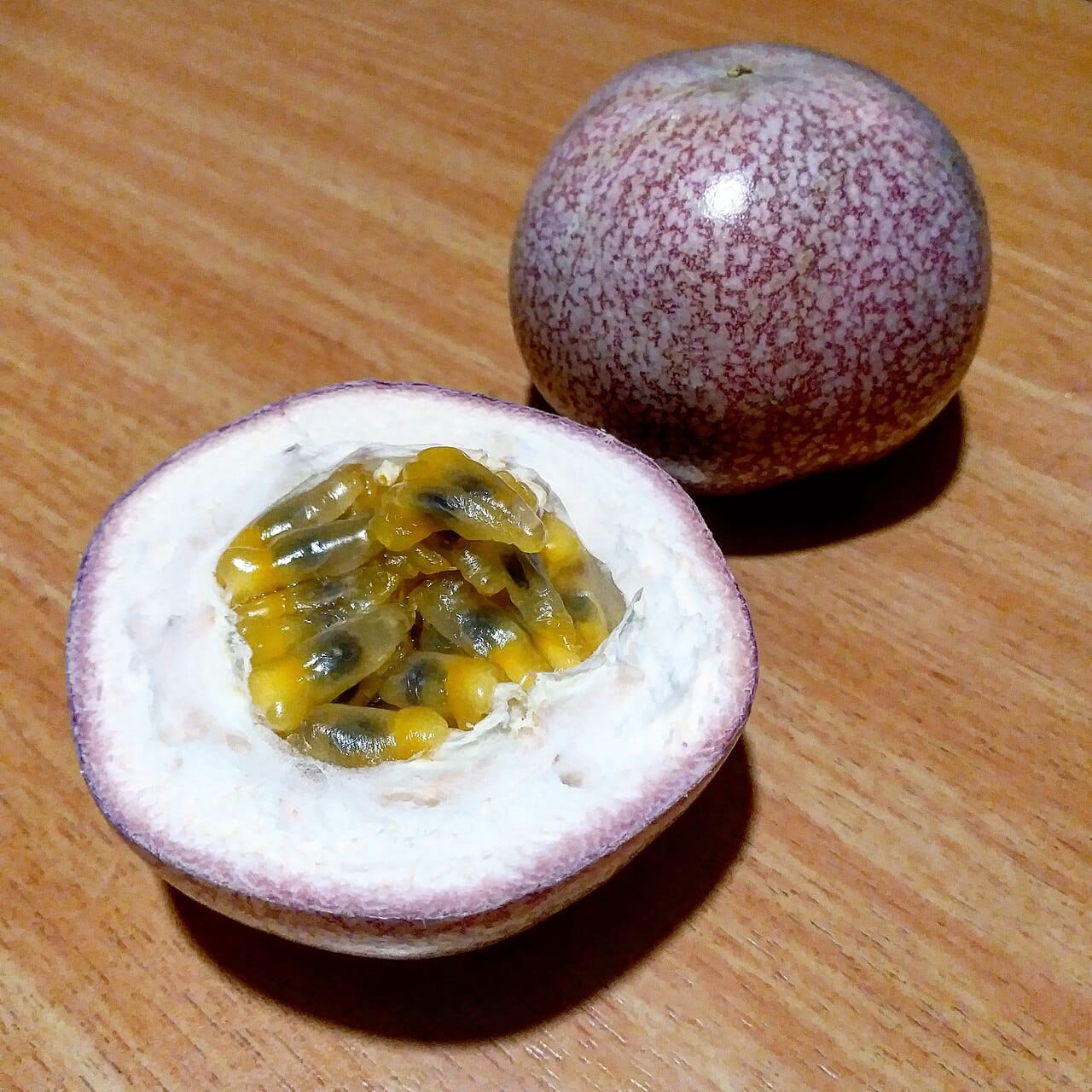 Passion Fruit : Le Trésor Tropical qui Éveille les Sens 2 Fruit de la passion entier et coupé en deux dévoilant sa pulpe jaune aux graines noires